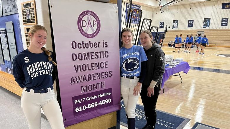 Three female students stand next to a banner that says October is Domestic Violence Awareness Month.