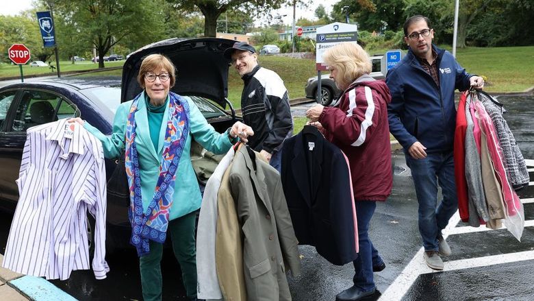 A man takes clothing out of a car trunk and hands it to three other adults.