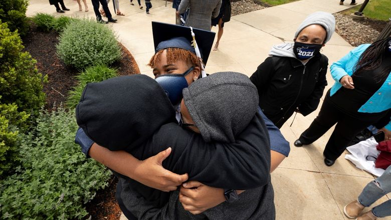woman in mask and graduation cap hugging two people