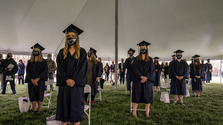 Graduates in caps and gowns standing under large white tent.