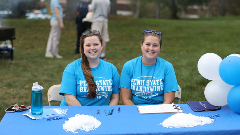 Two Penn State Brandywine volunteers sit at the registration table at the 2019 homecoming celebration.