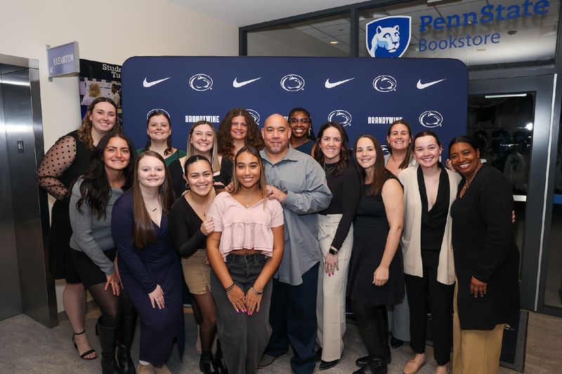 a group of people standing for a photo in front of a penn state backdrop