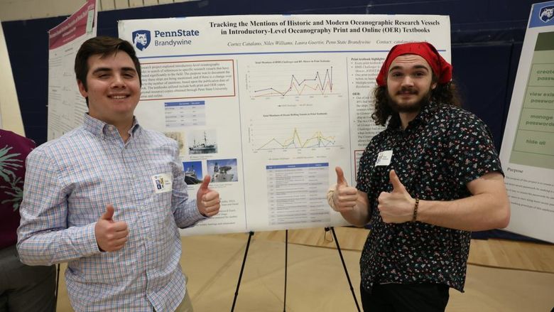 Two men giving thumbs up in front of research poster