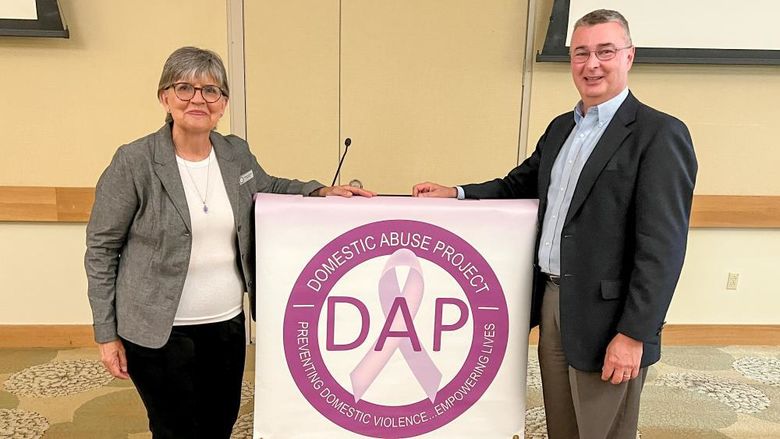 A woman and a man stand next to a lectern with a Domestic Abuse Project banner in the center.