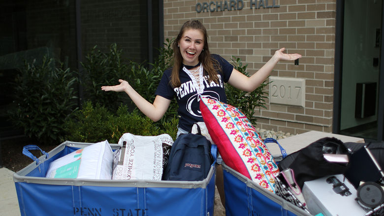 female student standing in front of Orchard Hall with bins to move in