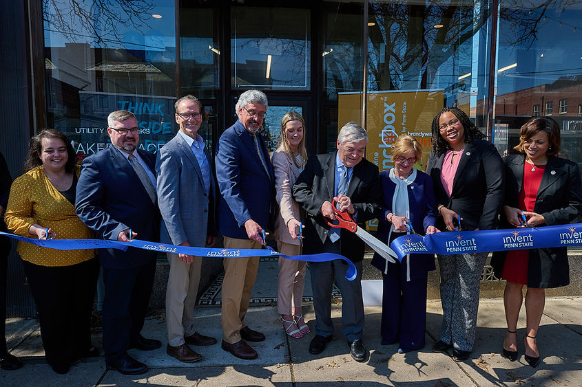 A group of 9 people cuts a long ribbon in front of a building.