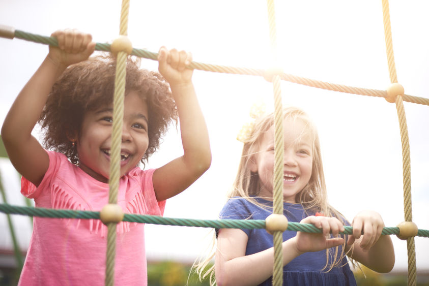 Two small children smiling and climbing on a rope course