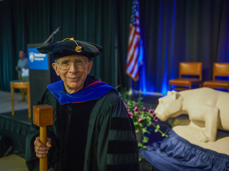 A man wears academic regalia and holds a mace.